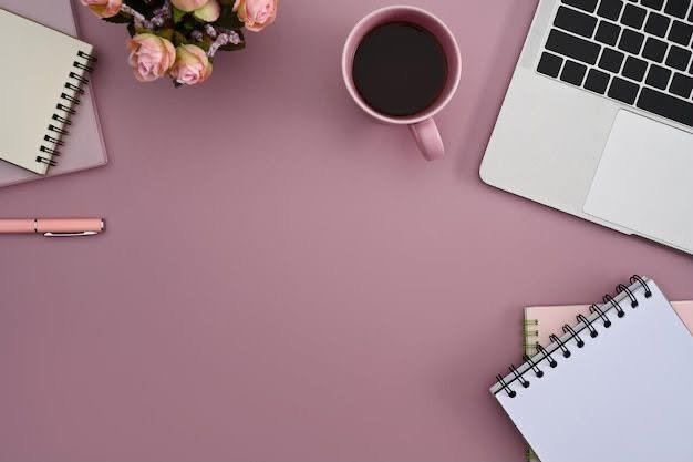 Pink aesthetic desk setup top view with laptop, notebooks, coffee cup, and flowers⁠